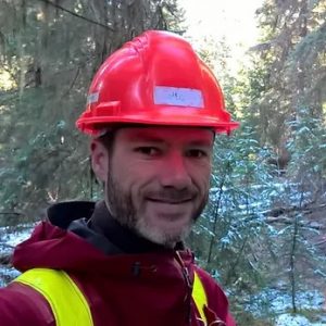 Greg wearing a hard hat and cruise vest, working in a snowy forest
