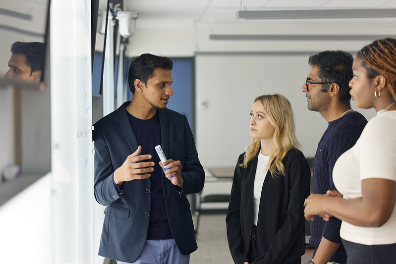 a group of 4 people talking in front of a whiteboard