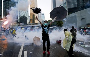 A protester raises his umbrellas in front of tear gas which was fired by riot police to disperse protesters blocking the main street to the financial Central district outside the government headquarters in Hong Kong