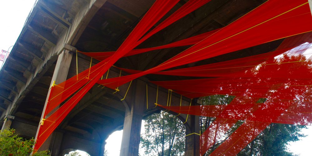 Looking up at an art installation under the Burrard Bridge featuring large swatches of fabric