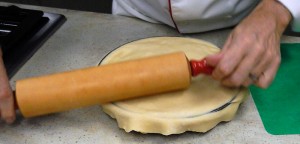 trimming the pastry crust by pressing down hard on the edges of the pie plate with a rolling pin