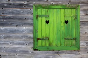 Bright green shutters on an old wooden builsing; a heart cut from each