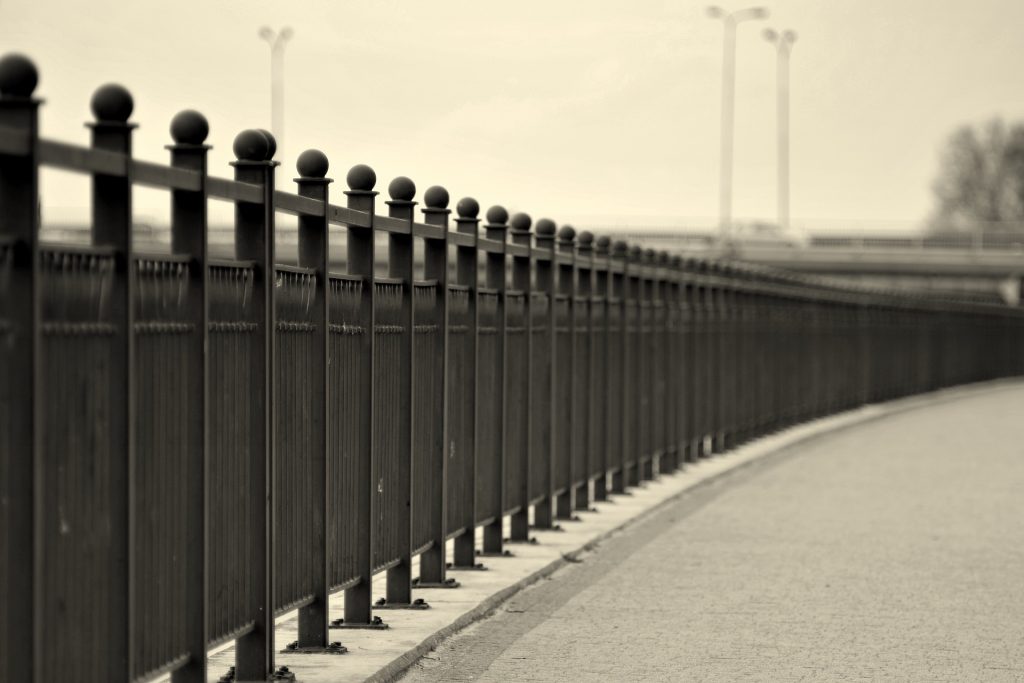 black and white image of a fence along an urban road