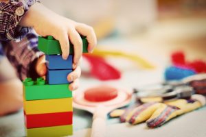 A child's hand puts together a tower of legos.