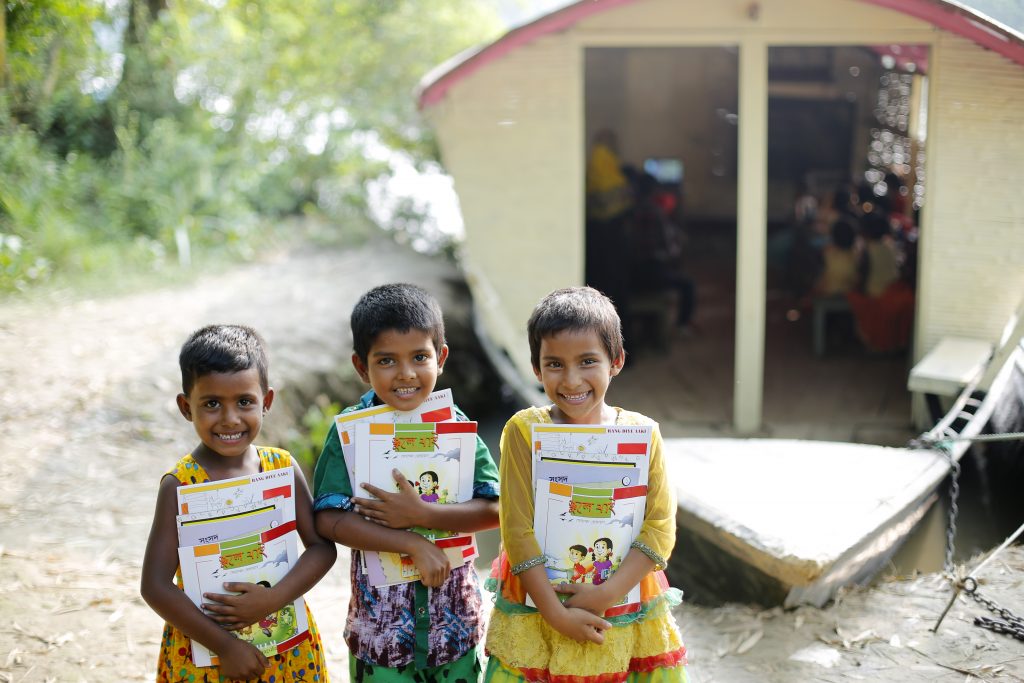 Three students smile standing in front of the Boroda Nagar Uttor Para Boat School, Chatmohor, Pabna.