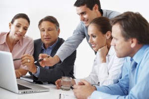 Happy business colleagues working together and discussing project on laptop during meeting