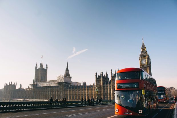 Red double decker bus passing by Palace of Westminster in London