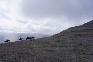 Group of six riders going up a ridge on horseback. Misty, cloudy background.