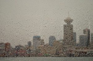 depicted is a view of Vancouver's skyline obstructed by rain in the foreground on a window.