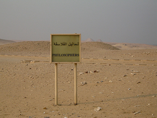 desert in the background with a sign that says "philosophers" in English with Arabic letters on top of that