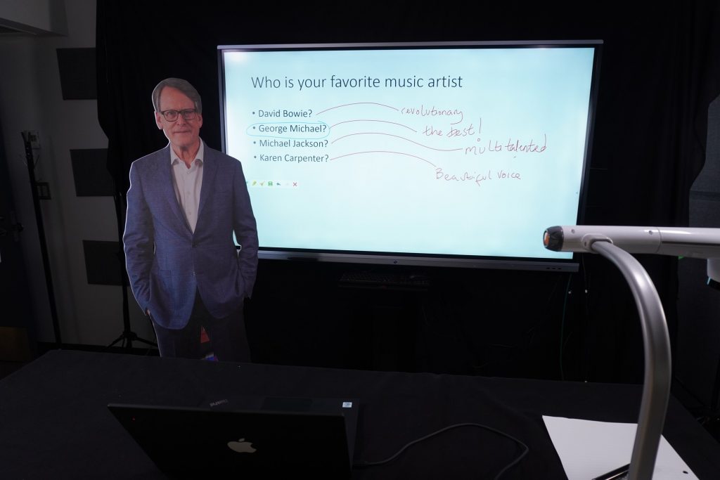 An image showing the LOFT screen, a document camera, and part of the table in front of the LOFT, as well as a cardboard cutout of a person for scale.