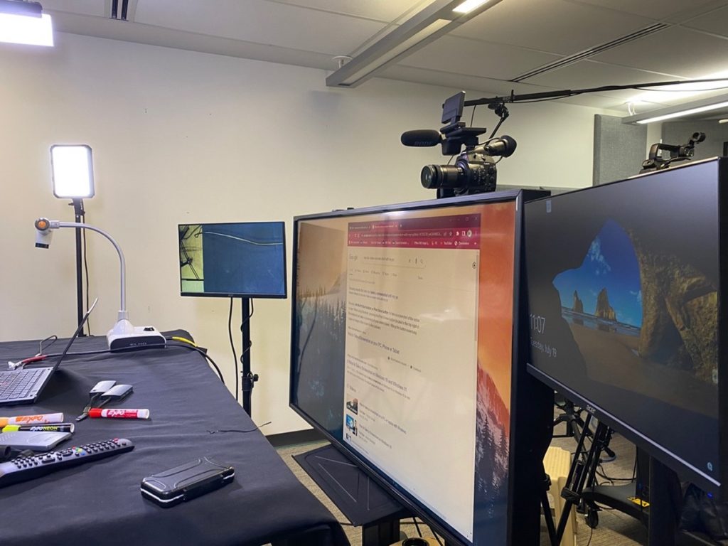 An image showing the other side of the LOFT setup. Three monitors are shown, as well as the document camera and part of the table. The camera and microphone sit on top of the middle monitor.