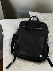 A black backpack is perched up on a white and grey background